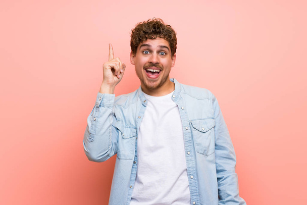 Blonde man over pink wall intending to realizes the solution while lifting a finger up - Photo, image