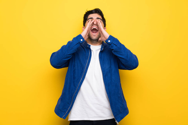Man with blue jacket over yellow wall shouting and announcing something - Photo, Image