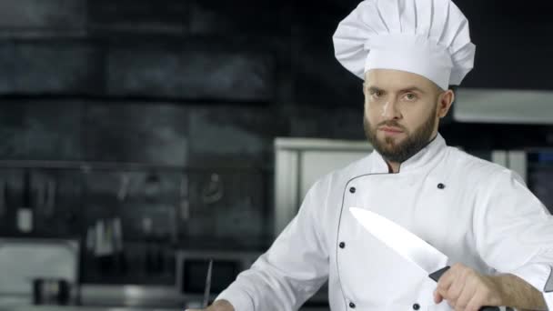 männlicher Koch posiert mit gekreuzten Messern. Koch schärft Messer in der Küche. - Filmmaterial, Video