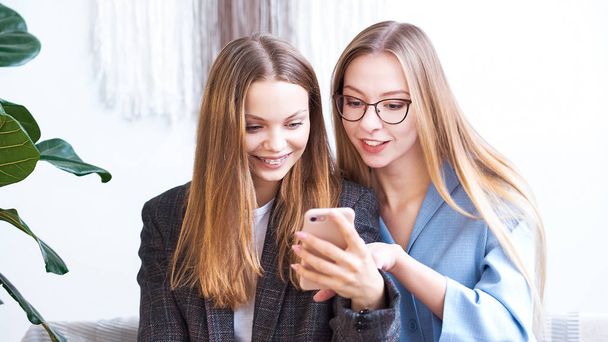 Surprised two young women blogger chatting with best friends in social network on mobile phone while received shocking good news using wifi zone and reading interesting book indoors after work - Zdjęcie, obraz