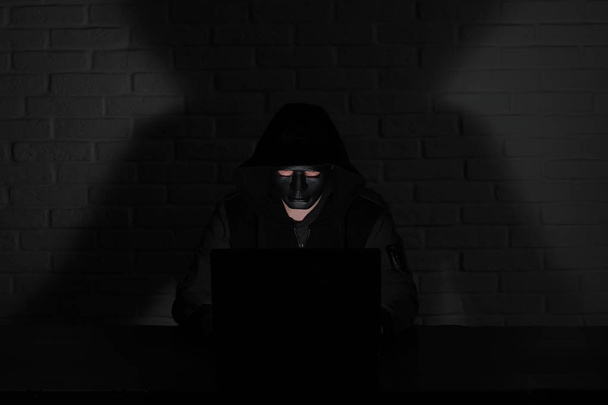 Hacker in zwart masker en capuchon aan de tafel - Foto, afbeelding