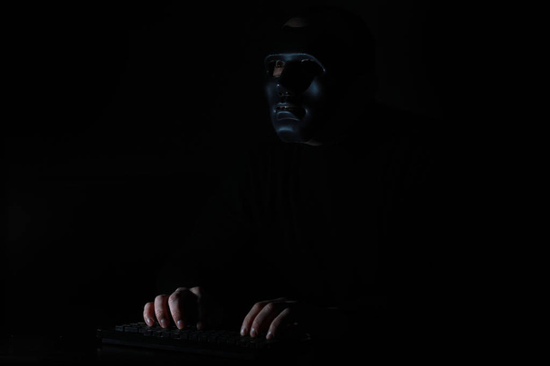 A man in a mask prints on the keyboard in the dark - 写真・画像
