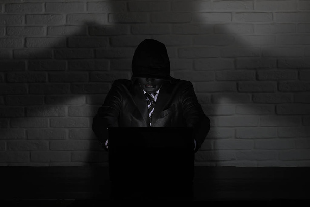 Hacker in black mask and hood at the table - Foto, Bild