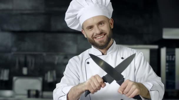 Küchenchef hat Spaß mit Messern in der Küche Lächelnder Koch schärft gekreuzte Messer - Filmmaterial, Video