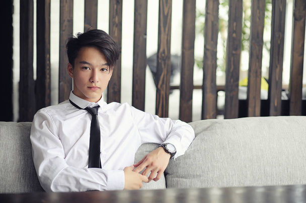 Молодой азиатский бизнесмен ждет партнера в кафе. Корейский юноша разговаривает по телефону в кафе - Фото, изображение