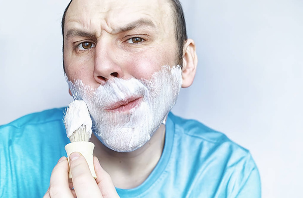 Un homme se rase devant un miroir. Mousse à raser. Rasoir jetable
. - Photo, image