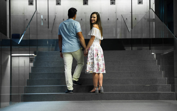 ハイテク建築様式のモダンな建物の中を歩いている若い家族。ファッションカップル現代的な建物ホールを歩く。二人は階段を上がって先へ - 写真・画像
