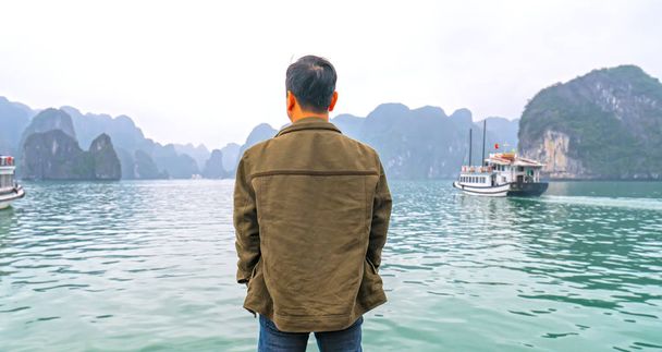 Hombre de vista trasera viajero en barco mirando la bahía de Halong en Vietnam entre las islas
. - Foto, imagen