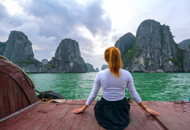 Back view kadın gezgin Halong Bay, Vietnam adalar arasında rahat görünümlü teknede oturan. - Fotoğraf, Görsel