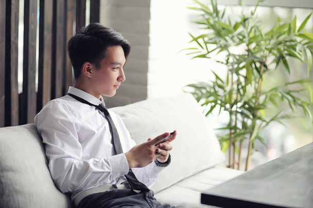 Un giovane uomo d'affari asiatico sta aspettando un partner in un caffè. Un giovane coreano che parla al telefono in un caffè - Foto, immagini