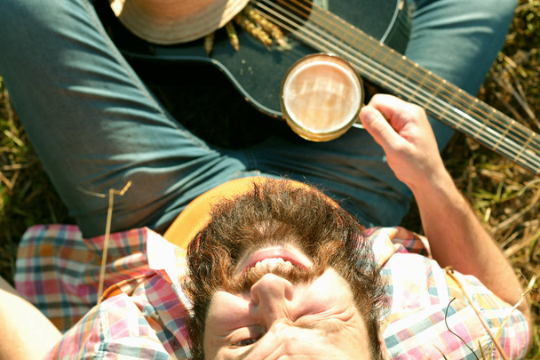 homem com guitarra e cerveja na natureza
 - Foto, Imagem