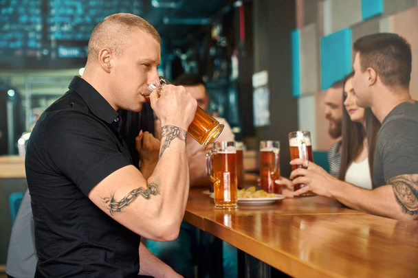 Strong tattooed man sitting drinking beer in pub - Photo, Image