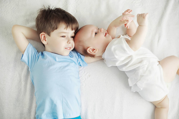 Дети лежат на кровати рядом с новорожденным ребенком, младшая сестра
. - Фото, изображение