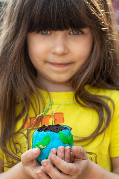 Χαριτωμένο κοριτσάκι προστατεύουν τον κόσμο. Σώσε την έννοια της γης. Εστίαση στον πλανήτη με πράσινο φυτό.  - Φωτογραφία, εικόνα