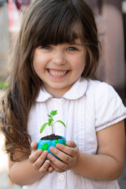 Cute little girl protect world. Save the earth concept. Focus on planet with green plant.  - Фото, изображение