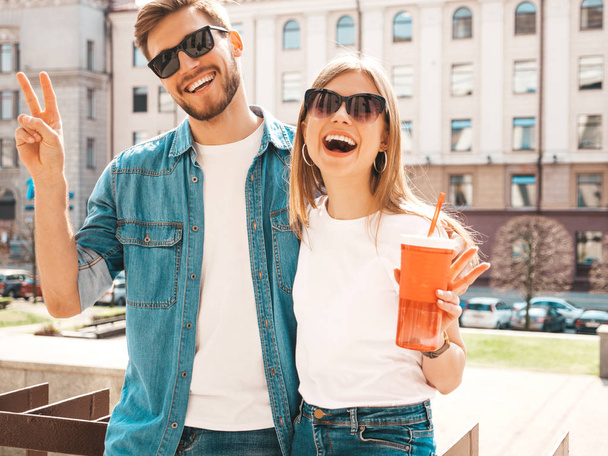Portrait of smiling beautiful girl and her handsome boyfriend in casual summer clothes. Happy cheerful family having fun on the street background in sunglasses. With bottle of water and straw - Foto, afbeelding