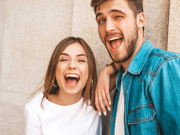 Portrait of smiling beautiful girl and her handsome boyfriend in casual summer clothes. Happy cheerful family having fun on the street background. Hugging and winking - Photo, image