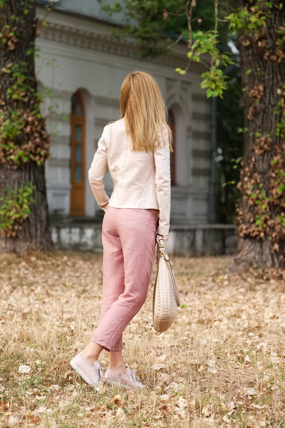 Unrecognizable girl in linen trousers and beige leather jacket walking on ground covered with fallen leaves - Valokuva, kuva