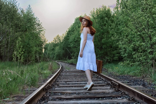 chica en un vestido blanco y maleta de mimbre caminando sobre rieles
 - Foto, Imagen