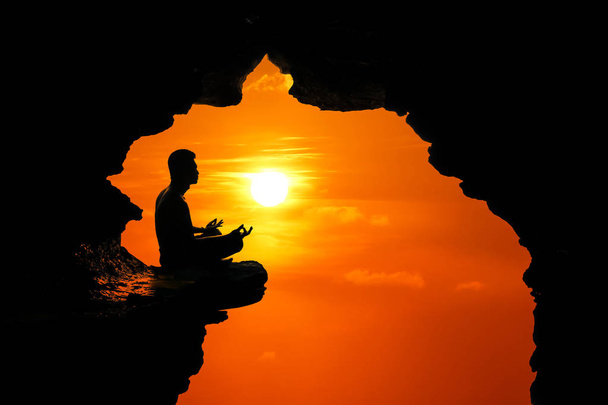 Man meditatie en bidden in de grot op de hoge klif op zonnen - Foto, afbeelding