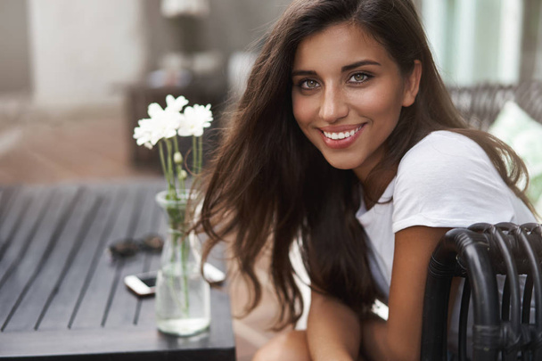 Gorgeous hispanic tanned young woman giggle flirty turn camera smiling joyfully sitting outdoor coffee table hanging out friends hotel restaurant near beach, order cold beverage nice warm weather - Photo, image