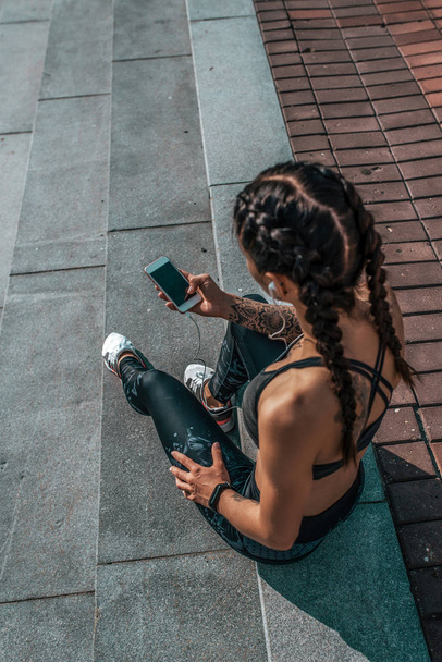 Girl athlete sitting steps resting after workout fitness summer city, day morning. Sportswear, smart phone, headphones. Active lifestyle, motivation power. Internet application, music. - Foto, afbeelding