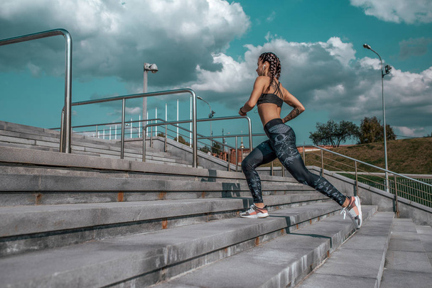 Girl athlete woman, runs on stairs, in summer city, free space, fitness workout, day and morning. Sportswear, leggings top sneakers. Active lifestyle, motivation power. Internet application, music. - Фото, изображение