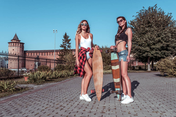 Two girlfriends girls, women sisters, posing in summer in the city, skate board, casual wear shorts swimsuit shirt. The concept of a weekend getaway, fashion style, modern lifestyle. Free space. - Foto, Imagem