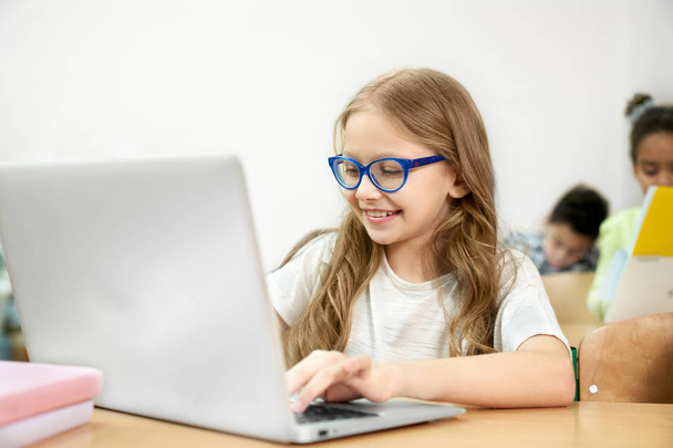 Schoolgirl at desk in classroom working in laptop. - Фото, зображення