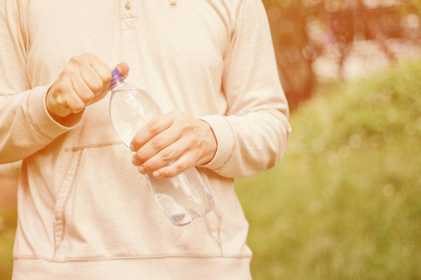 hombre hipster sosteniendo una botella de plástico con agua en la naturaleza. estilo de vida saludable, verano, calor. Caminar por el parque
. - Foto, Imagen