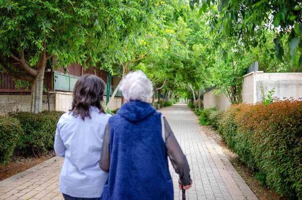Fortgeschrittener Psychotherapeut verwendet eine innovative Lösung in der Arbeit mit einer älteren Frau. zur vereinbarten Zeit spricht sie mit dieser Seniorin, während sie durch ihr Wohnviertel läuft. - Foto, Bild