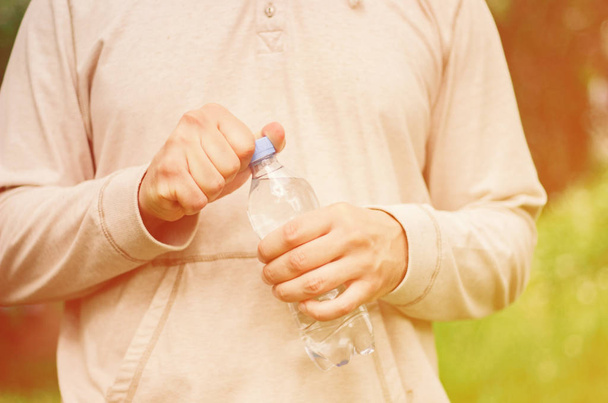 Mann Hipster hält eine Plastikflasche mit Wasser in der Natur. Gesunder Lebensstil, Sommer, Hitze. Spaziergang im Park. - Foto, Bild
