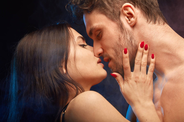 dark-haired woman with red manicure touching her mans face and kissing him - Foto, imagen