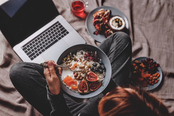 Woman in home clothes eating vegan Rice coconut porridge with figs, berries, nuts. Healthy breakfast ingredients. Clean eating, vegan food concept - Photo, Image