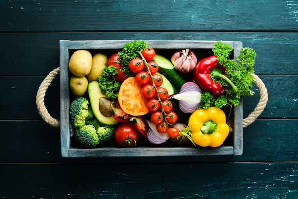 frisches Gemüse und Obst in einer Holzkiste. Avocados, Tomaten, Erdbeeren, Melonen, Kartoffeln, Paprika, Zitrusfrüchte. Ansicht von oben. Freiraum für Ihren Text. - Foto, Bild