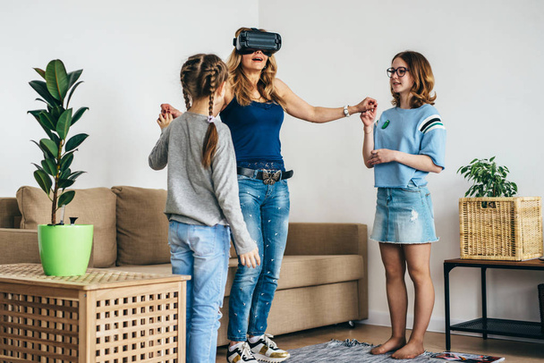 Жінка використовує VR окуляри віртуальної реальності вдома, стоячи на вітальні з дітьми
. - Фото, зображення