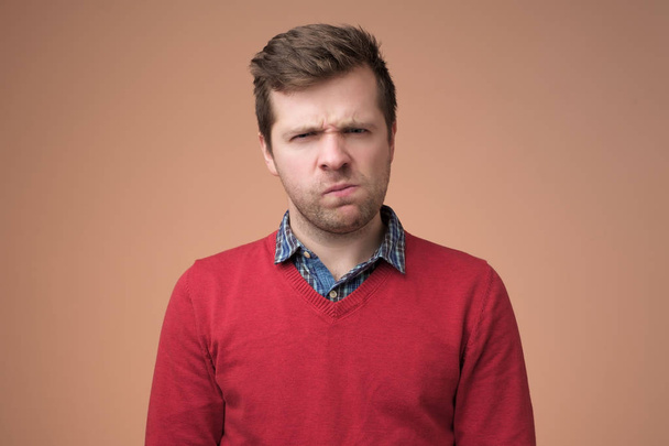 зрілий чоловік в червоному светрі дивиться з виразом недовіри
 - Фото, зображення