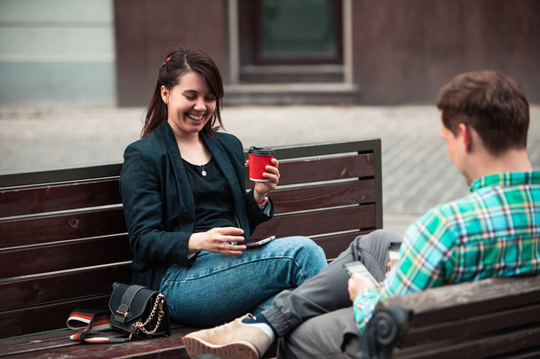 χαμογελαστός ζευγάρι που κάθεται στο παγκάκι και μιλάει ο ένας στον άλλο πίνοντας καφέ - Φωτογραφία, εικόνα