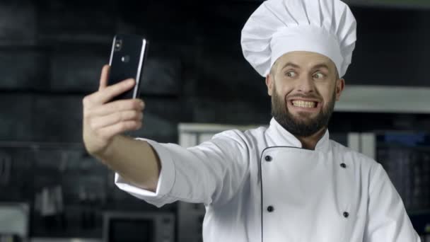 Profesjonalny szef kuchni stwarzając w kuchni. Chef podejmowania selfie zdjęcie z telefonem komórkowym - Materiał filmowy, wideo