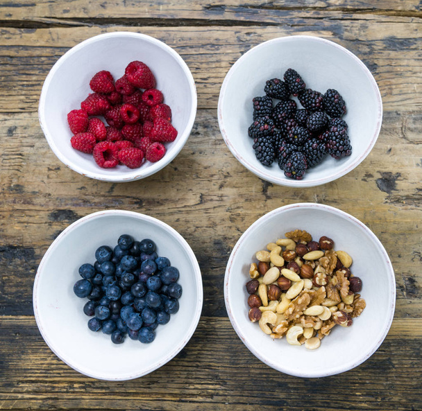 round white ceramic bowls with berries and nuts on a rustic wood - Foto, Imagem