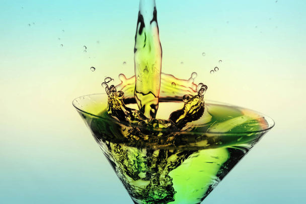 Beautiful splash of liquid from a martini glass on a blue gradie - Фото, изображение
