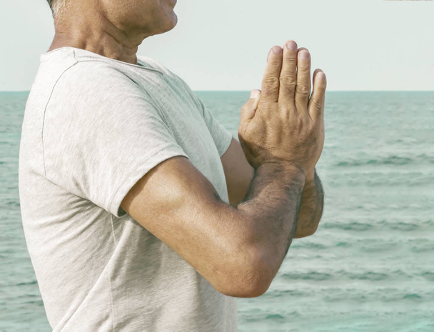 Un hombre adulto se para juntando sus palmas frente a él en un gesto namaste junto al mar
. - Foto, imagen