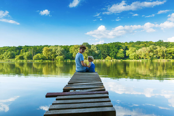 Father and a tiny girl in dungarees are sitting on the bridge an - 写真・画像