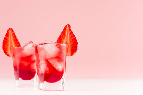Fresh summer strawberry homemade cocktails in two shot glasses with ice cubes, strawberry slice in elegant pastel pink color kitchen interior. - Photo, image