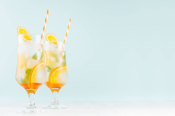 Juicy oranges lemonades with ripe sliced fruit, ice cubes, straw, green mint on elegant blue pastel color background, copy space. - Photo, image