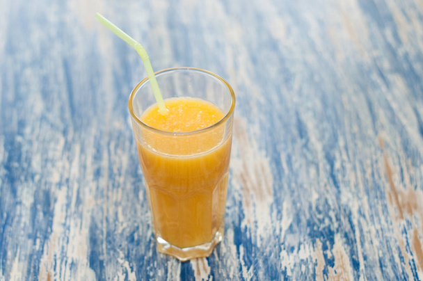 Χυμός πορτοκαλιού σε ένα ποτήρι με άχυρο σε μπλε ξύλινο φόντο από κοντινό-πράσινο - Φωτογραφία, εικόνα