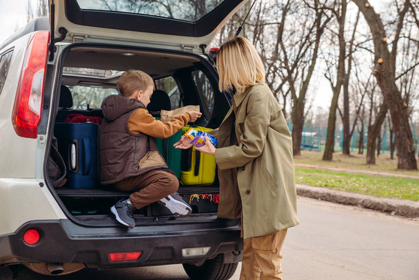 little kid sitting with mother in car trunk full of luggage eating chocolate candies - 写真・画像