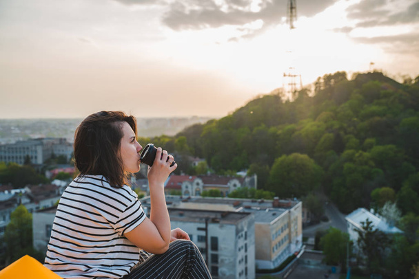 vrouw zitten op geel opblaasbare matras drinken koffie genieten van zonsondergang over de stad - Foto, afbeelding