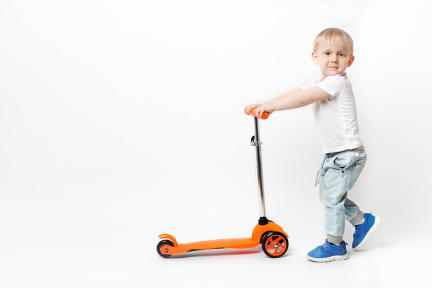 幼児の子供は白い背景のハンドルによってオレンジ色の明るいスクーターを転がす. - 写真・画像
