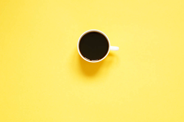 flach liegende Tasse schwarzen Kaffee auf gelbem Hintergrund. Minimalistisches Ernährungskonzept. - Foto, Bild